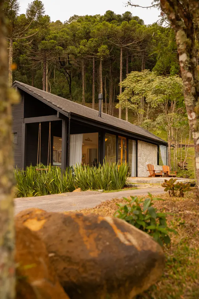 Cabana de madeira com telhado em duas águas entre árvores altas e jardim de folhagens